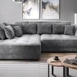 Canapé d'angle gris foncé avec des coussins rembourrés, placé dans un salon moderne avec des décorations murales abstraites et une plante verte à côté.