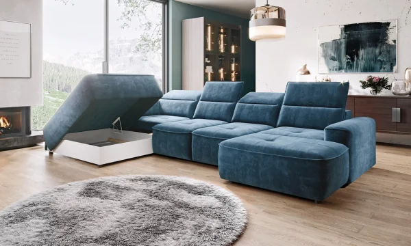 Canapé d'angle bleu avec compartiment de rangement ouvert, installé dans un salon moderne. Parquet en bois clair, cheminée allumée, grande baie vitrée avec vue sur la montagne, tapis rond en fausse fourrure grise, et éclairage suspendu contemporain.
