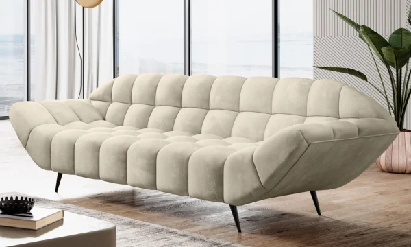 Zoom sur un canapé beige capitonné au design incurvé et moderne, avec des pieds noirs élégants, placé dans un salon lumineux face à de grandes baies vitrées.
