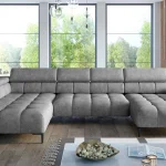 Canapé d'angle extra-large en tissu gris, doté d'appuie-têtes réglables et de pieds métalliques fins, situé dans un salon moderne baigné de lumière naturelle avec de grandes baies vitrées et une décoration épurée.